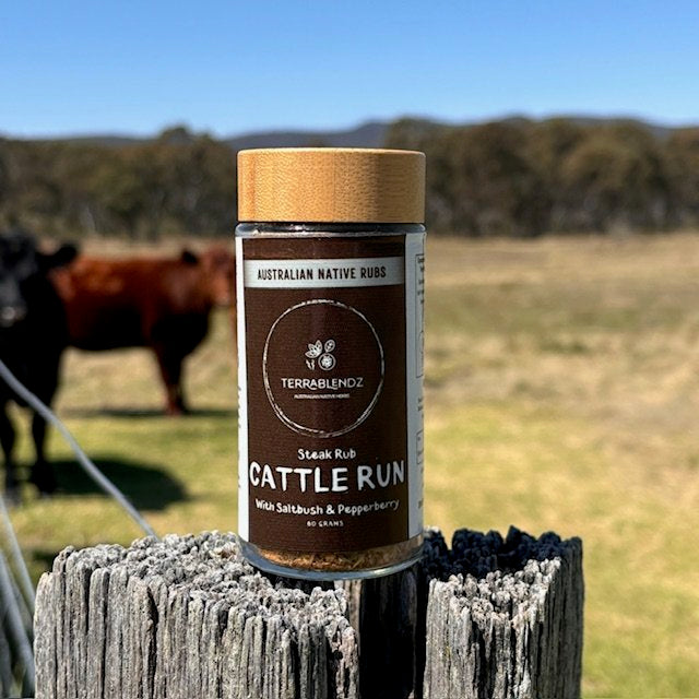 Native Spices Enhance Steak: Terrablendz Cattle Run Steak Rub on a farm post with cow in the background.